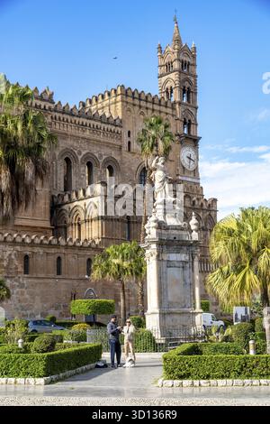 Palermo - Sizilien - Italien - 03-18-2025: Statue und Palmen vor dem Turm und der Fassade der Kathedrale von Palermo, mit zwei Personen und einem Hund Stockfoto
