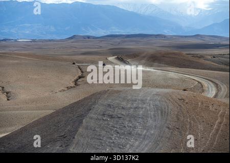 Kurvenreiche, unbefestigte Straße führt durch die karge Landschaft der Agafay-Wüste in Marokko Stockfoto