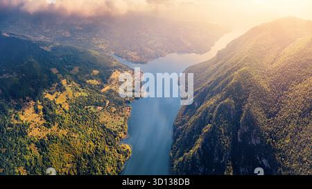 Der Fluss schlängelt sich durch ein tiefes Tal, umgeben von üppigen grünen Wäldern und Bergen bei Sonnenuntergang, Sonnenlicht reflektiert auf dem Wasser Stockfoto