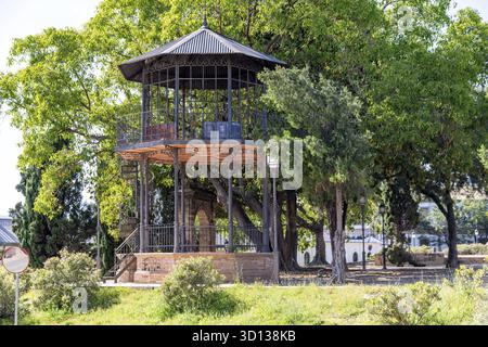 Jerez de la Frontera, Cadiz - Spanien - 23.04.2024: Ein zweistöckiger Metallpavillon mit kunstvollen Geländern, umgeben von üppigen Bäumen. Eine Wendeltreppe führt Stockfoto
