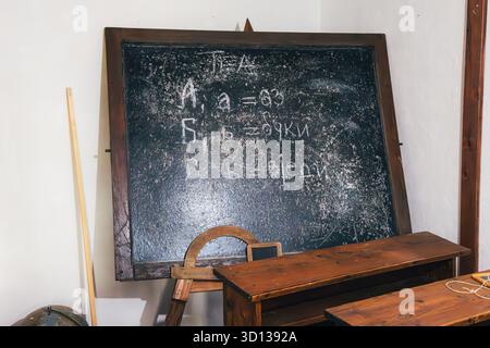 Vintage-Klassenzimmer-Szene mit einer verstörten Tafel mit handgeschriebenem kyrillisch-slawischem Alphabet und alten hölzernen Schülerpulten Stockfoto