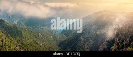 Panoramablick aus der Luft mit Bergen und einem Talsee, umgeben von üppig grünen Wäldern, mit Wolken und Nebel Stockfoto