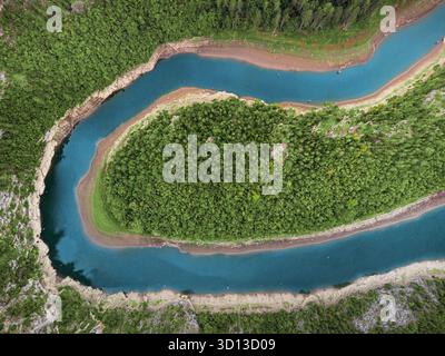 Aus der Vogelperspektive zeigt einen natürlichen Fluss, der sich durch einen dichten Wald schlängelt und von trockenen Ufern umgeben ist Stockfoto