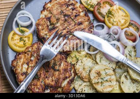 Gehacktes Hähnchenkotelett mit gegrilltem Gemüse liegt auf einem Teller. Gegrilltes Geflügel und Gemüse. Wunderschönes Essen. Speiseplan. Braten Stockfoto