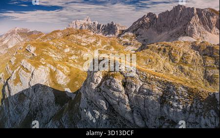 Weitläufige Berglandschaft mit steilen Felsformationen, grasbewachsenen Hängen und dramatischen Schatten unter einem dynamischen Himmel Stockfoto