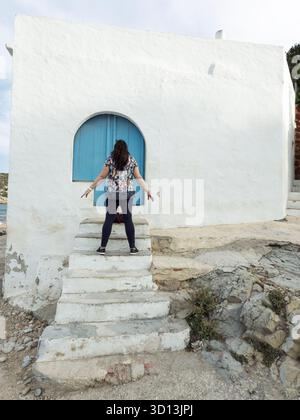 Frau, die auf einer alten, weiß getünchten Treppe vor einer blauen Bogentür steht Stockfoto