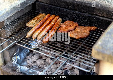 Würstchen und Steaks werden auf dem Rost auf einem alten, rustikalen Grill gekocht, der selektiv auf den Punkt kommt Stockfoto
