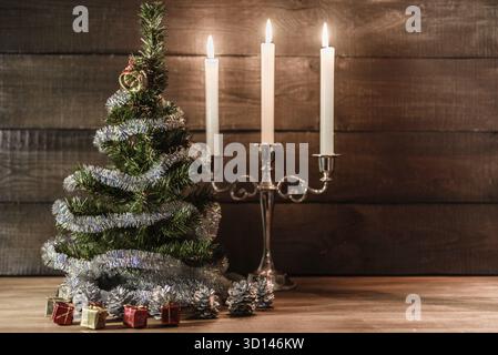 Weihnachten, dekorativer Baum mit Regen geschmückt ist, steht auf dem Tisch mit Kerzen Stockfoto