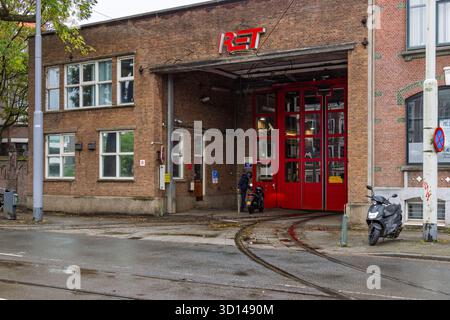 Der Eingang zu einem historischen Backsteingebäude, das als RET-Straßenbahndepot in Rotterdam dient, mit großen roten Türen und sichtbaren Straßenbahnschienen auf der nassen Straße Stockfoto