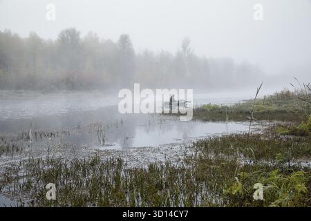 Ein Mann in einem Boot, der im Nebel auf dem See schwimmt Stockfoto