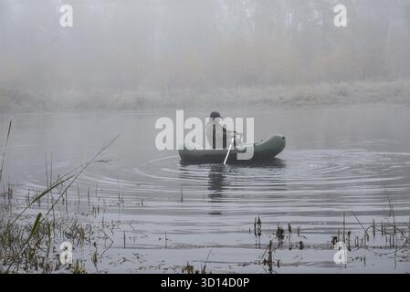 Ein Mann in einem Boot, der im Nebel auf dem See schwimmt Stockfoto