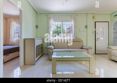 Komfortabler Loungebereich mit weichen Möbeln, grünen Wänden, gefliestem Boden und Zugang zum Schlafzimmer und zur Eingangstür Stockfoto