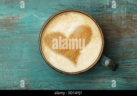 Nahaufnahme einer vollen Cappuccino-Tasse mit herzförmigem Latte Art-Schaum auf grunge-blauem Tafel, Kopierraum, Hochwinkelansicht, direkt darüber Stockfoto