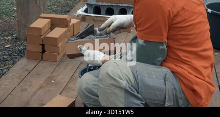 Ein Mann baut eine Mauer. Brick hat die Lösung aufgesetzt. Bau eines Backsteinhauses Stockfoto