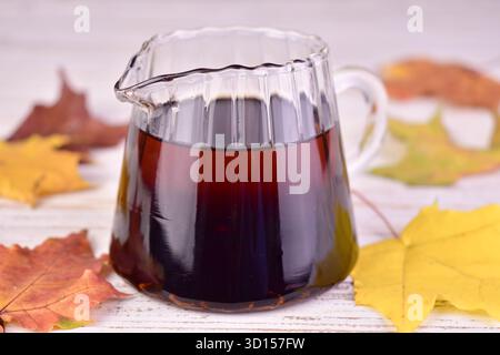 Ahornsirup in einem Glas-Soße-Boot vor dem Hintergrund herbstlicher Ahornblätter. Stockfoto
