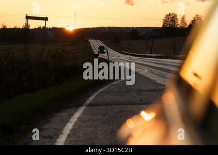 Hollola, Finnland - 13. September 2025 - Straße, die sich bei Sonnenuntergang in Richtung Horizont erstreckt, über eine ruhige ländliche Landschaft im herbstlichen Abendlicht. Stockfoto