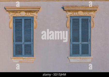 Zwei geschlossene blaue Fenster an der pastellfarbenen Wand Stockfoto