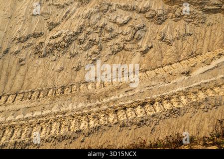 Frische Baggerreifen auf sandigen Hängen mit Erosion und strukturiertem Boden unter warmem Sonnenlicht. Selektiver Fokus. Stockfoto