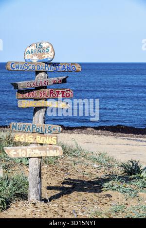 SArchittu - Sardinien - Italien - 03-02-2025: Hölzerne Wegweiser mit farbenfrohen Wegweisern an einem Sandstrand mit blauem Meer und klarem Himmel in SArchittu Stockfoto