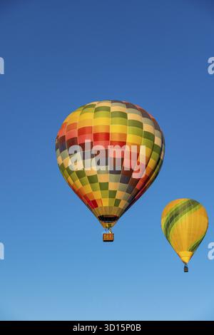 Guadix, Granada - Spanien - 24.01.2024: Zwei bunte Heißluftballons steigen in den klaren blauen Himmel. Einer hat ein buntes kariertes Muster, der andere ist y Stockfoto