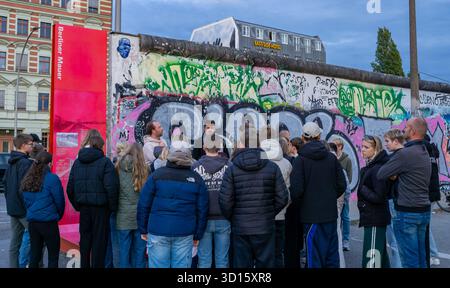 Eine Gruppe von Touristen hört einem Reiseleiter in der Berliner Wall East Side Gallery in Berlin, Deutschland. Stadttourismus, Gruppe von Touristen, Tourgruppe. Stockfoto