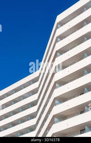 Abstraktes modernes weißes Hotelgebäude mit eckigen Balkonen und Glasgeländern vor einem klaren, tiefblauen Himmel, C'an pastilla mallorca Stockfoto
