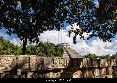 Die Pyramide von El Castillo, eingerahmt von Bäumen mit den Schädelschnitzereien von Tzompantli im Vordergrund, Chichén Itzá. Stockfoto