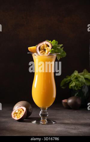 Passionsfrucht und Mangococktail oder Saft in Hurrikanglas auf schwarzem Hintergrund. Vertikales Format. Traditionelles gesundes Getränk mit Mango. Frische Lassi aus Joghurt, Wasser, Gewürzen, Obst und Eis. Stockfoto