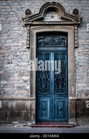 Verzierte Vintage-blaue Holztür mit schmiedeeisernen Details in einem Steingebäude mit klassischen architektonischen Elementen Stockfoto