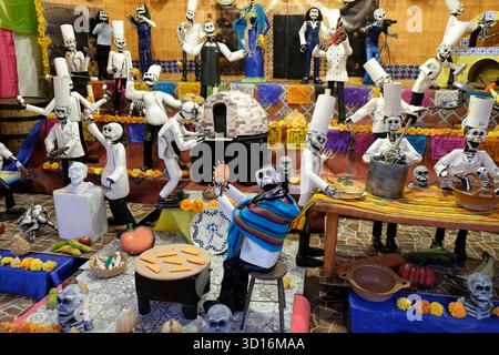 Farbenfrohe Ausstellung zum Tag der Toten mit Skelettfiguren, die als Köche und Musiker gekleidet sind, umgeben von Ringelblumen und traditionellen Dekorationen Stockfoto