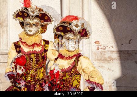 Paare in komplizierten Gesichtsmasken und farbenfrohen rot-goldenen Kostümen, Karneval von Venedig, Venedig, Venetien, Italien Stockfoto