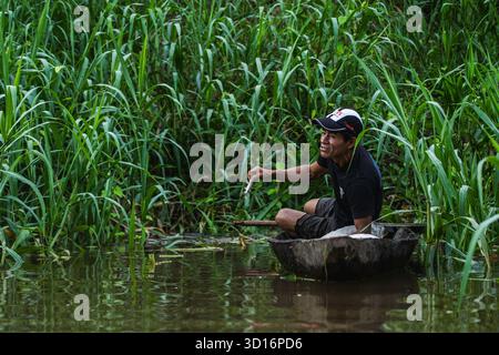 Ein einheimischer Mann fängt Fisch auf einem traditionellen Holzkanu durch dichte Vegetation an einem kleinen Nebenfluss des Amazonas in der Nähe von Nauta, Loreto, Peru, 2024. Stockfoto