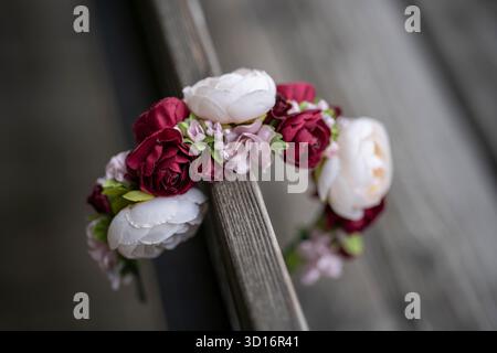 Blumenkranz aus bunten Blumen, die auf der Rückenlehne einer Holzbank mit verschwommenem Hintergrund hängen, Konzept der Tradition und Erinnerung. Stockfoto