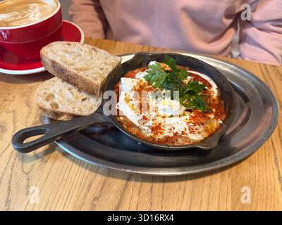Shakshuka mit Brot, serviert in einer Eisenpfanne. Mediterraner Geschmack, Frische und hausgemachter Komfort im Café-Frühstücksgericht. Stockfoto