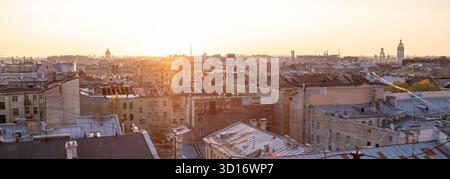 Wenn die Sonne untergeht, wirft warmes Licht einen goldenen Farbton über die Dächer von St. Petersburg und beleuchtet die einzigartige Architektur der Stadt vor einem klaren Himmel. Stockfoto