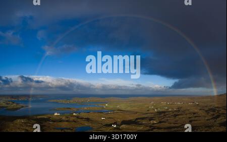 Panoramablick auf einen Regenbogen über Uig Sands auf der Isle of Harris, Äußere Hebriden, Schottland, mit verstreutem Sonnenlicht und dramatischem Himmel. Stockfoto
