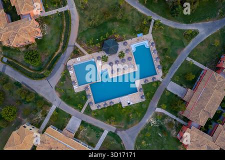 Von oben aus der Drohne blickt man auf einen wunderschönen Resortkomplex, geometrischen Swimmingpool, Sonnenliegen und Ferienvillen mit roten Dächern. Mediterrane Unterkünfte Stockfoto