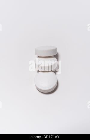 Arzneimittel, drei runde weiße Tabletten auf weißem Hintergrund, übereinander angeordnet. Stockfoto