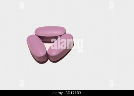 Medikamente, drei längliche rosa Pillen auf weißem Hintergrund, die sich gegenseitig berühren. Stockfoto