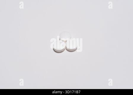 Arzneimittel, drei runde weiße Tabletten auf weißem Hintergrund, die in Kontakt miteinander und auf dem Boden angeordnet sind. Stockfoto
