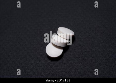 Medikamente, drei runde weiße Tabletten auf schwarzem Hintergrund, eine übereinander angeordnet und vor schwarzem Hintergrund. Stockfoto