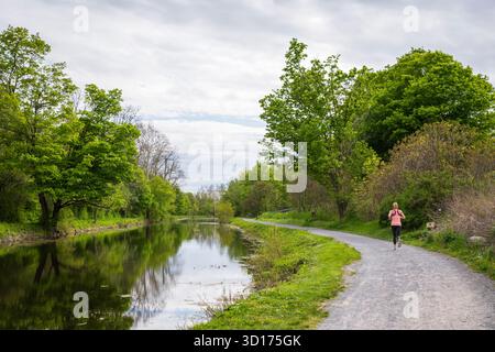 Camilus, NY USA - 18. Mai 2019: Frau läuft auf einem Pfad entlang des Nine Mile Creek Aqueduct, einem restaurierten Abschnitt des Erie Canal. Stockfoto