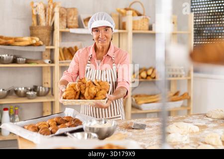 Porträt einer fröhlichen älteren Bäckerin mit Croissants Stockfoto