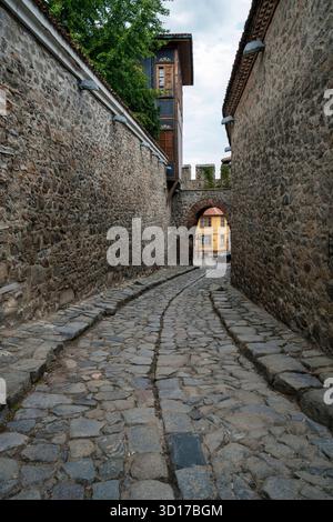 Historische kopfsteingepflasterte Straße und bogenförmiges Steintor, bekannt als Hisar Kapia in der Altstadt von Plovdiv, umgeben von mittelalterlichen Mauern und traditionellen Häusern. Stockfoto
