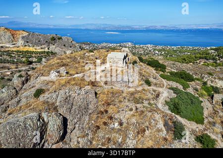 Mittelalterliche Steinkapelle auf dem felsigen Hügel von Palechora mit Blick auf das blaue Meer und die Küsten der Insel Ägina, Griechenland, mit Panoramablick. Stockfoto