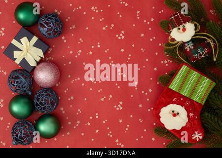 Weihnachtsbaumzweige, Kugeln und eine blaue Geschenkbox mit goldenem Band auf rotem Hintergrund, festliche Weihnachtskomposition Stockfoto