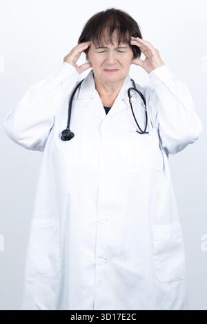 Frustrierte Ärztin im weißen Mantel mit Stethoskop, die ihre Schläfen vor starken Kopfschmerzen hält, erschöpft und von Stress überwältigt Stockfoto