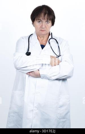 Eine Ärztin trägt einen weißen Labormantel und Stethoskop, steht mit überkreuzten Armen und vermittelt Professionalität Stockfoto