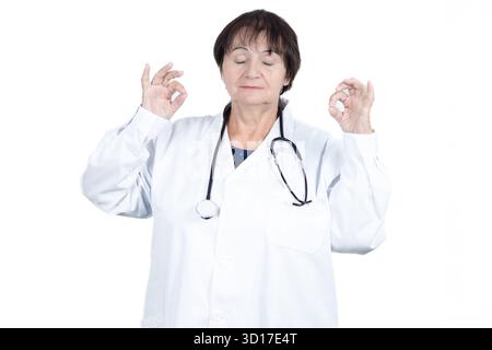 Eine Ärztin mit weißem Labormantel und Stethoskop meditiert mit geschlossenen Augen und findet Ruhe und Frieden mit Mudra-Hand-Geste Stockfoto