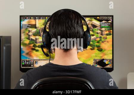 Ganz nah an den Hinterbliebenen eines Mannes, der ein Gamer-Kopfkoffer benutzt und einen Bildschirm mit dem Strategie-Videospiel Age of Empires 2 auf einem pc ansieht Stockfoto